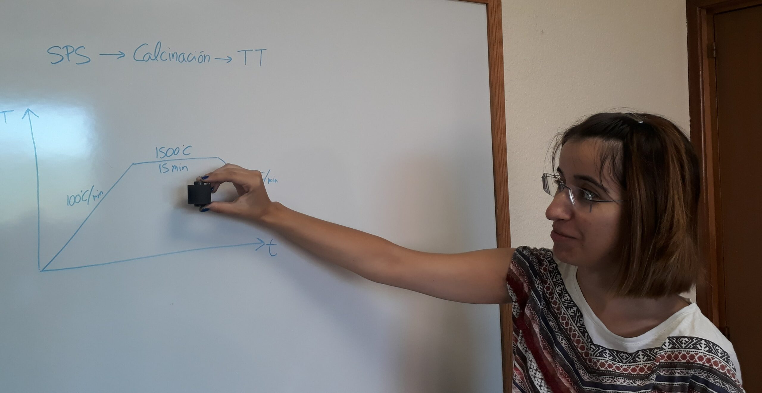 La investigadora Manuela González muestra el molde para la preparación de la muestra junto a las condiciones de trabajo en la pizarra
