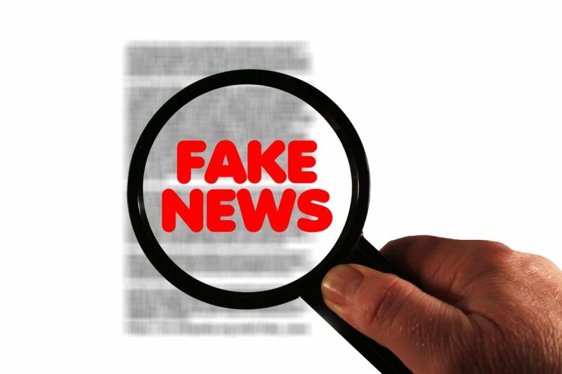 Lupa negra sobre fondo blanco que destaca letras rojas que componen las palabras 'Fake News'